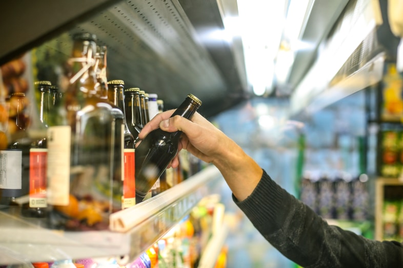 Close-up van een bierrek in een drankenwinkel waaruit een bierflesje wordt gehaald.